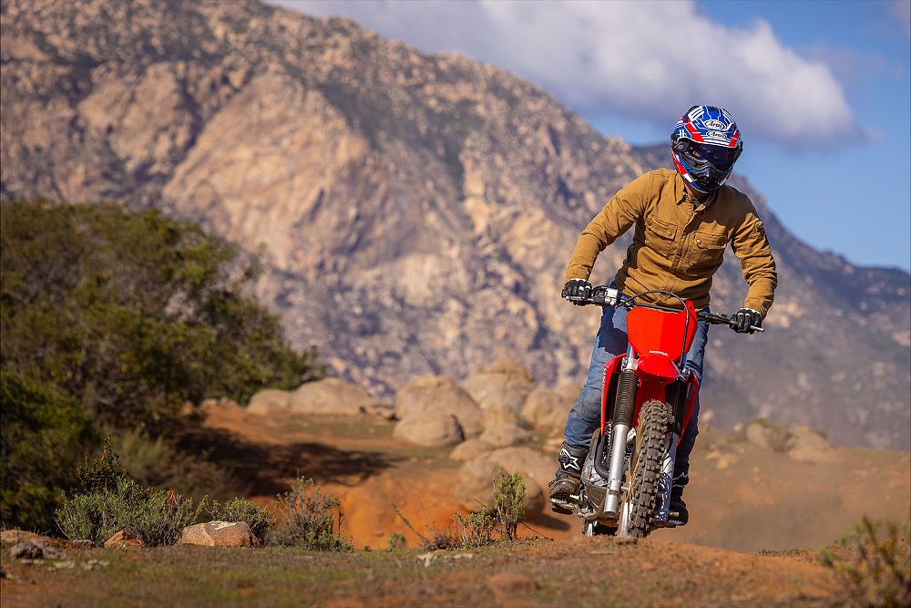 Dustin rides the CRF300F over the crest of a hill with a mountain in the background.