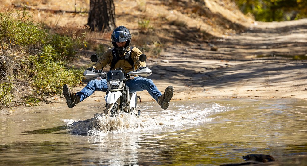 rider on a white Sherpa riding through a stream with feet up to keep them from getting wet