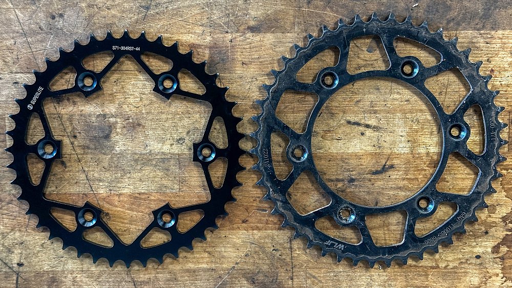 The Ibex 450's 47-tooth rear sprocket positioned next to a Superlite 44-tooth replacement on a workbench.