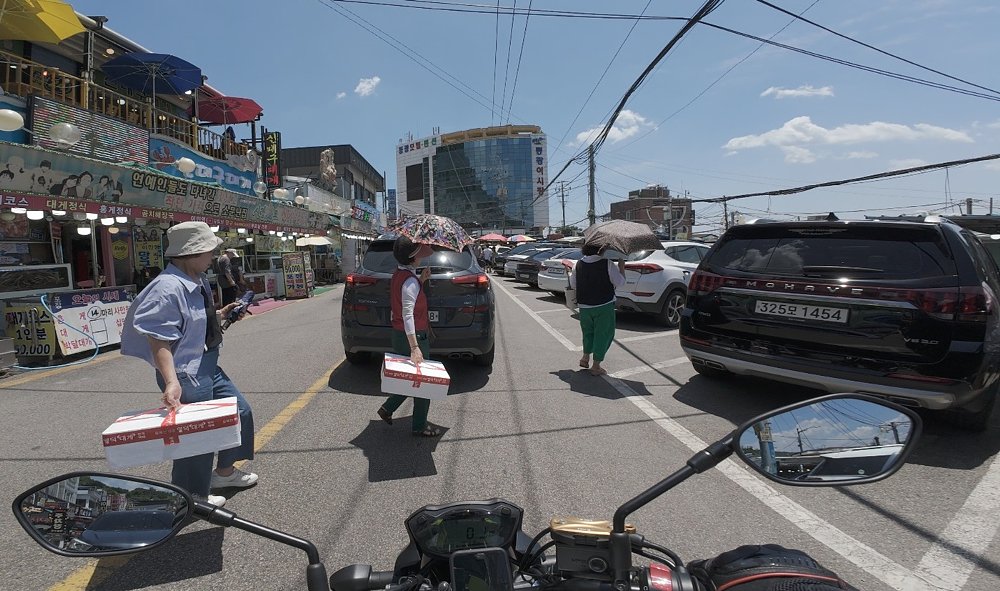 rider's view while stopped in a small village with pedestrians crossing the street carrying white foam coolers