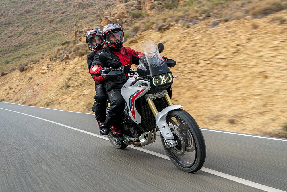 A couple rides the Ducati DesertX along a mountainous backroad.