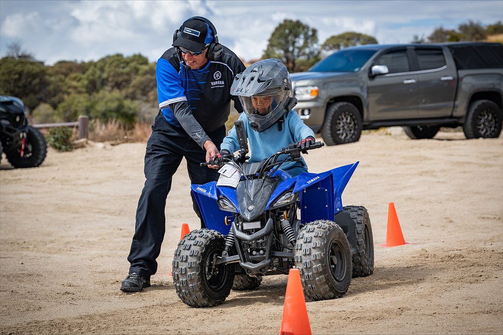 A Yamaha employee helps a young ATV rider navigate an off-road course.