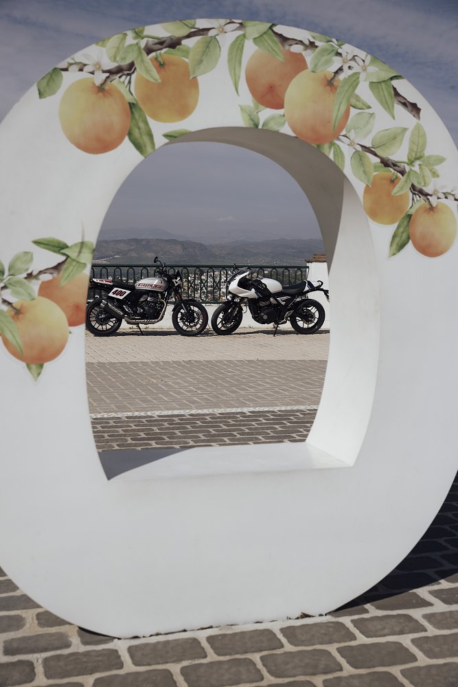 the two motorcycles at a mountainside area, framed by a large sculpture