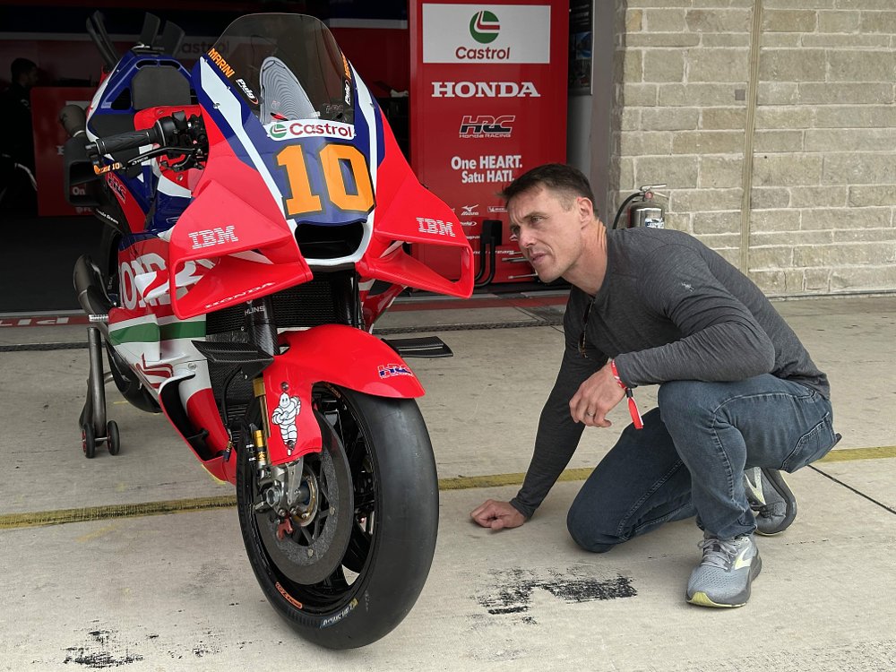 Ari Henning crouching down and looking closely at Honda's RC213V MotoGP racing motorcycle.