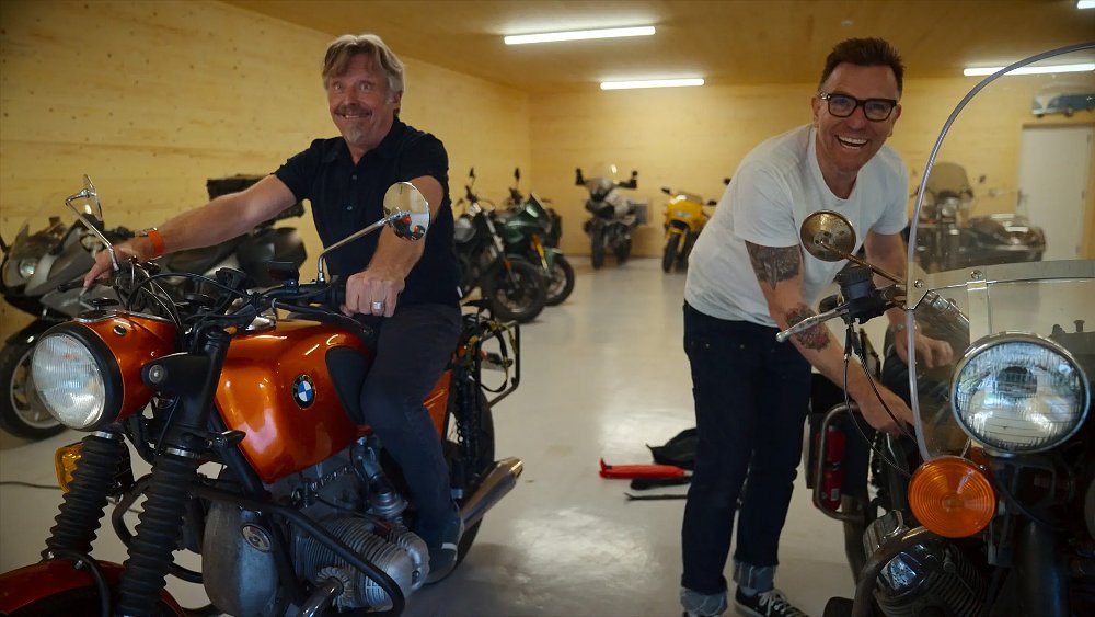 Charley Boorman and Ewan McGregor share a laugh while fiddling with their motorcycles.
