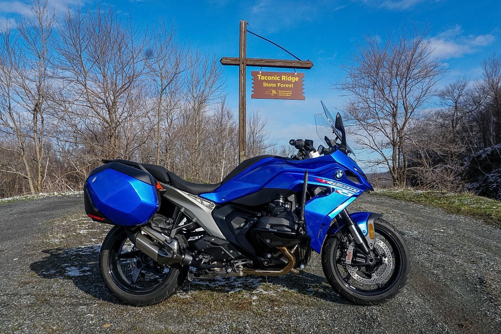 Blue BMW R 1300 RS parked at a mountain overlook underneath a Taconic Ridge State Forest sign