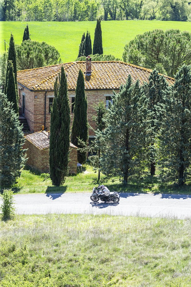 distant view of a motorcycle passing in front of a large country home in the green hills of Tuscany