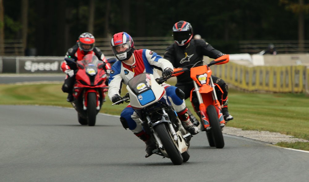 the author on his vintage Honda on the track, followed by an orange supermoto and a red sport bike