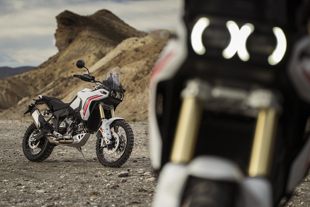 close view of the daytime running lights, shaped like parenthesis, around the two LED headlights, with a view of another full motorcycle in the background