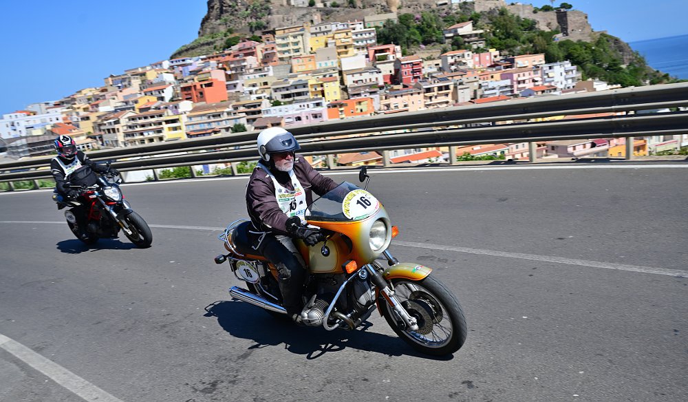 vintage motorcycles riding past a hillside village above the sea