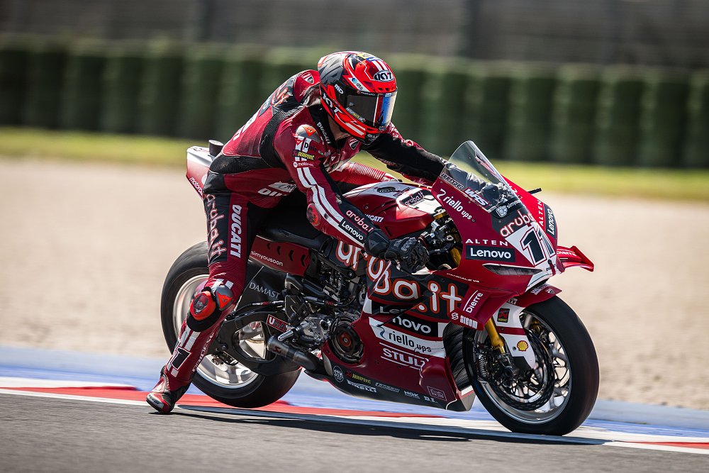 Bulega on his red Ducati race bike, braking hard into a corner with the rear tire rising off the pavement
