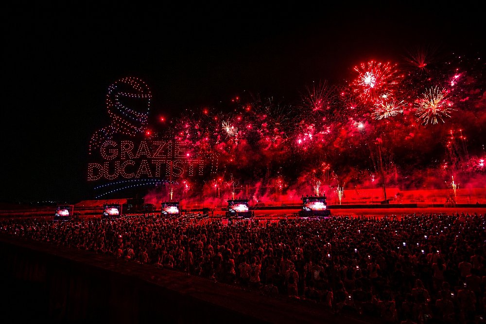 lighted drones forming the Ducati logo in the night sky as fireworks go off above the grandstands