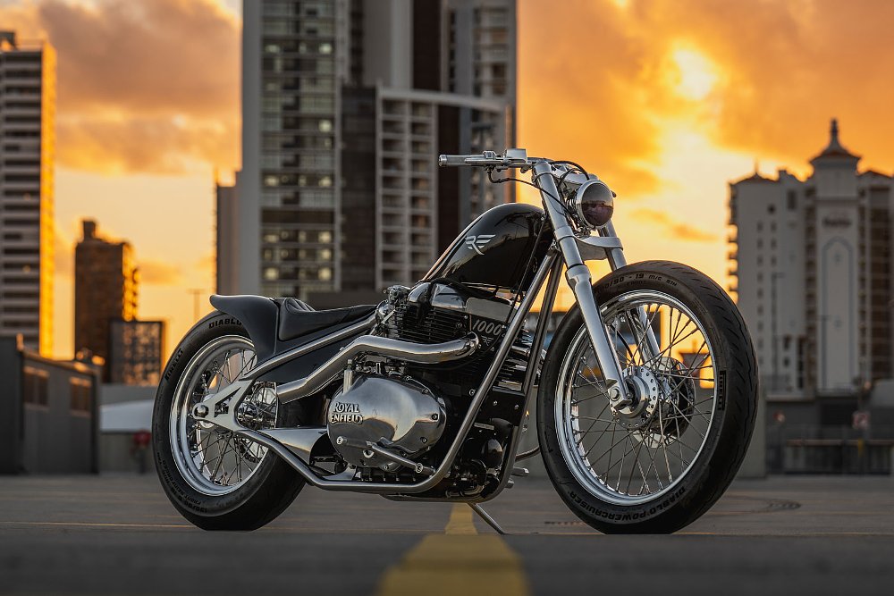 custom black Royal Enfield parked in front of a city skyline at sunset