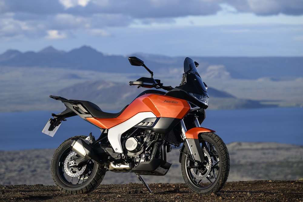 orange Norton Atlas parked in a wilderness area, lake and mountains in the distance