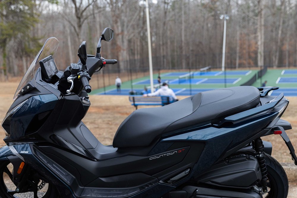 blue Kymco scooter parked at a park with tennis courts in the background