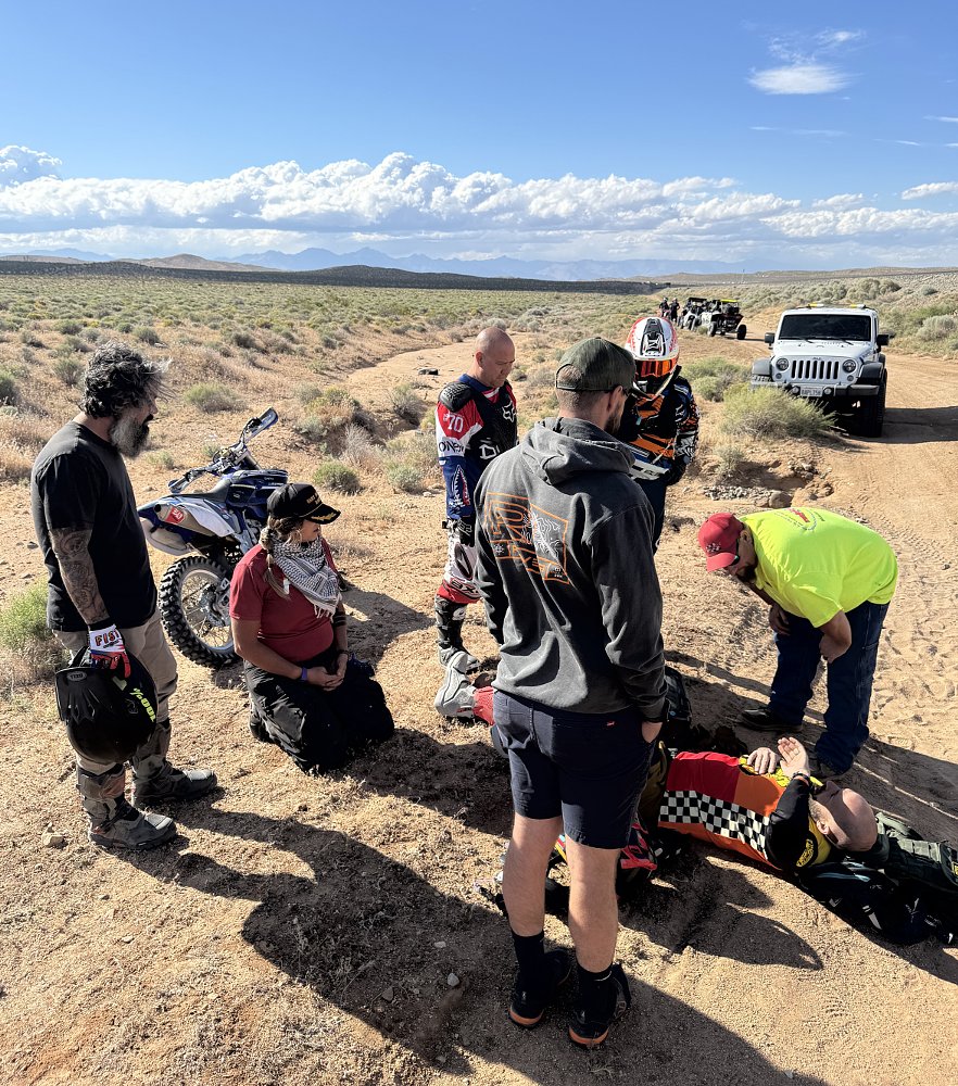 lying on the ground on a dirt desert road with others hovering around to help