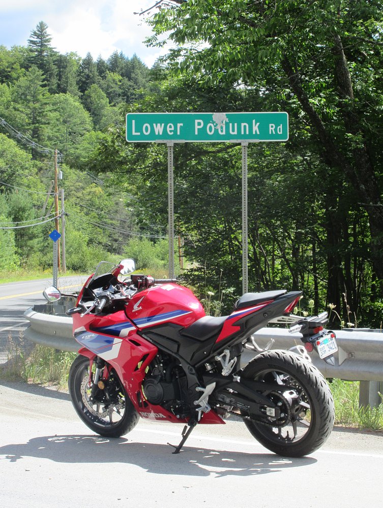 red CBR500R parked on a country road under a street sign that says 'Lower Podunk Road'