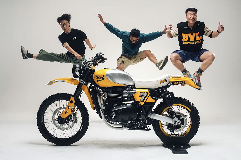 three members of the BVL crew leaping in the air behind the yellow custom motorcycle