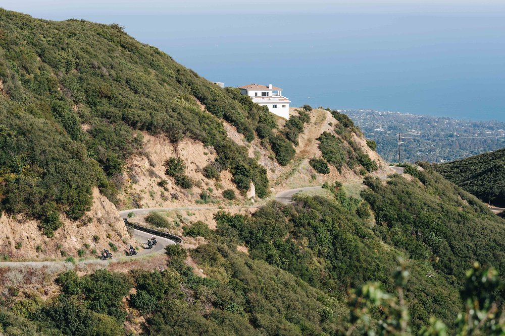 A twisty road winding along a mountainside with four motorcycles riding in the distance.