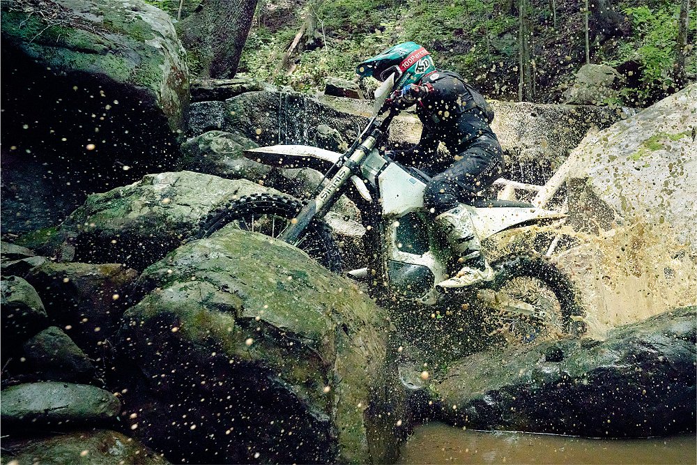 An 805 RX rider wheelies between a pile of boulders.