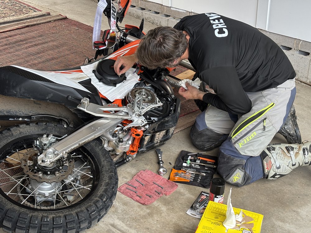 A 2026 KTM 690 Enduro R on its side in a garage, with a person working on the exposed clutch.
