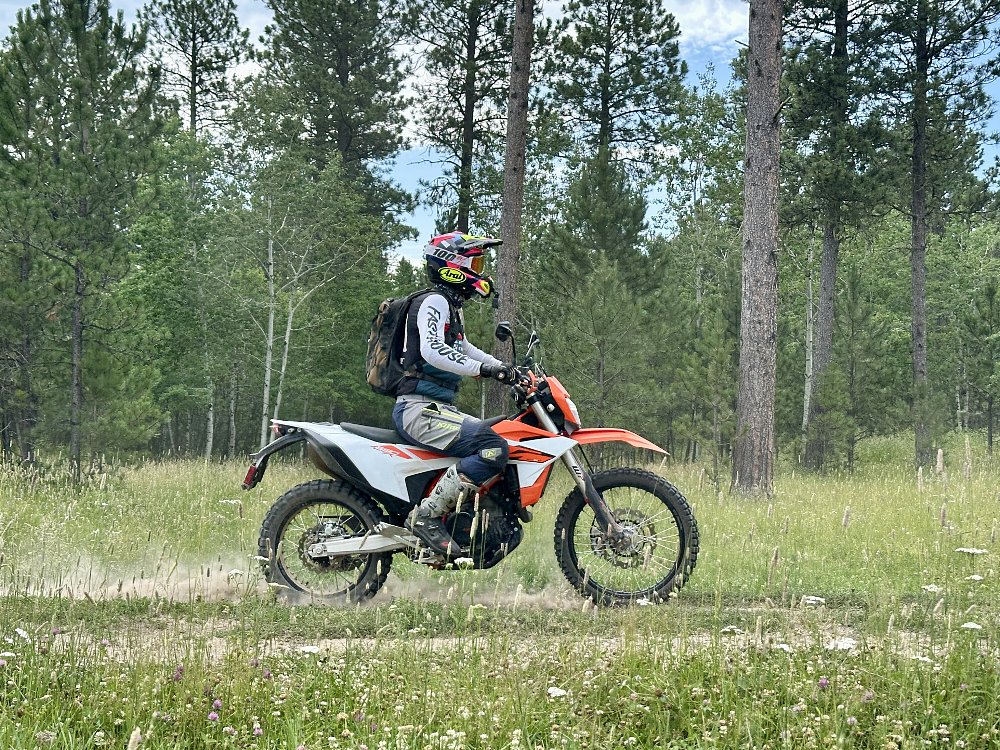 2026 KTM 690 Enduro R in profile, riding along a two-track road in a conifer forest.