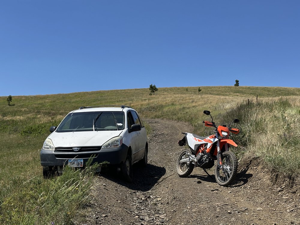 A 2026 KTM 690 Enduro R parked on a rural road next to an abandoned Toyota Sienna minivan.