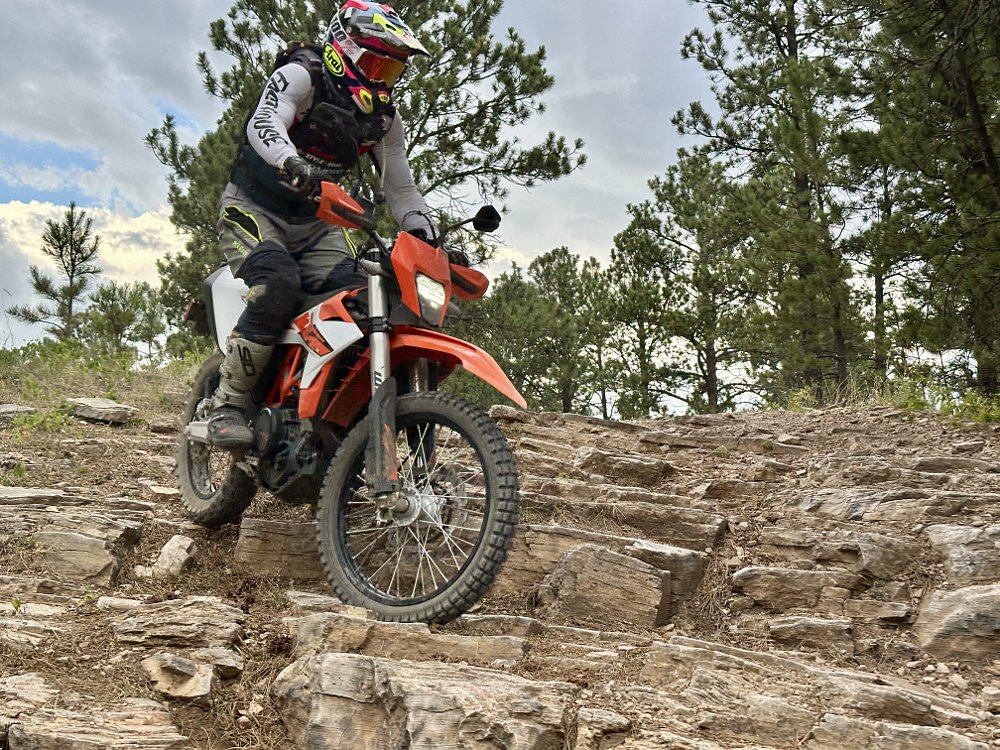 A 2026 KTM 690 Enduro R rides down a set of rock steps on a trail.