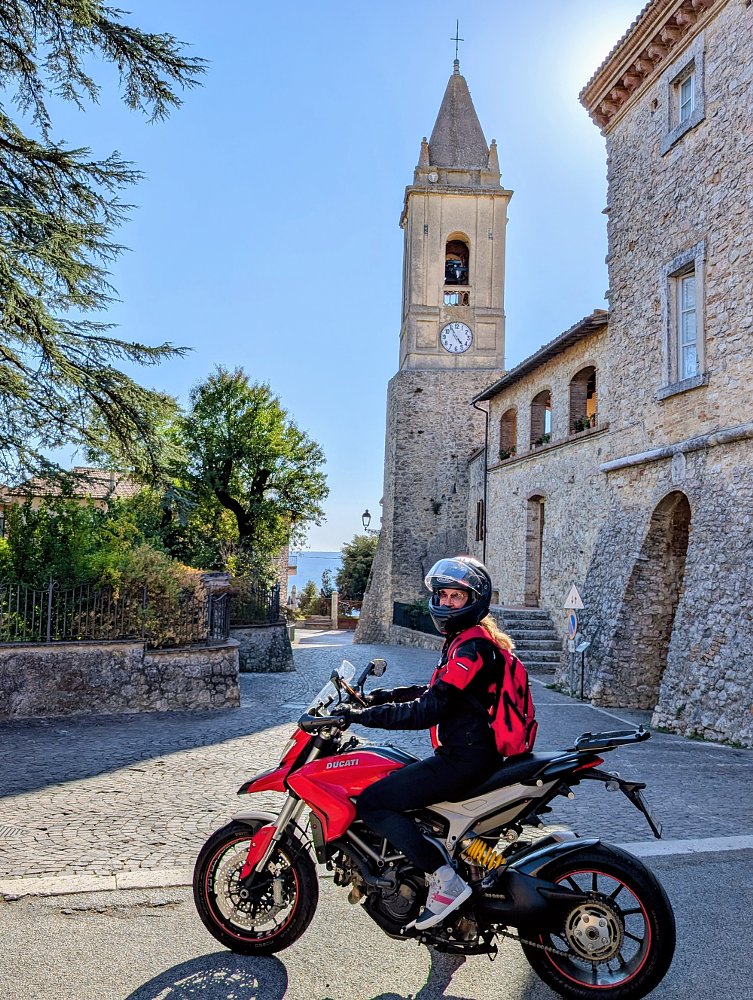 Wendy on the red Hyperstrada in front of an old stone church with a steeple in bright sunshine