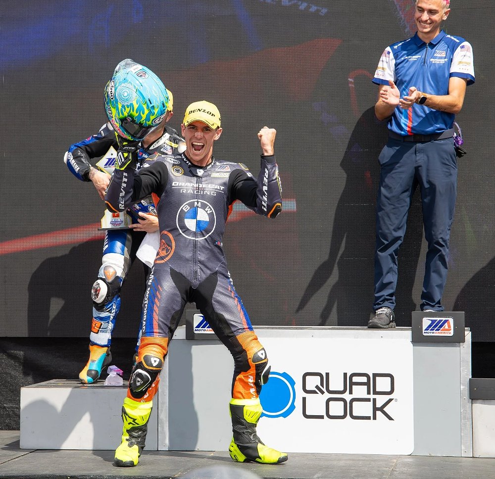 Sean Dylan Kelly holding a trophy, smiling, and raising a fist on the podium