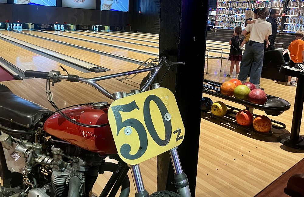 a motorcycle on display in the foreground as a child bowls on an alley in the background