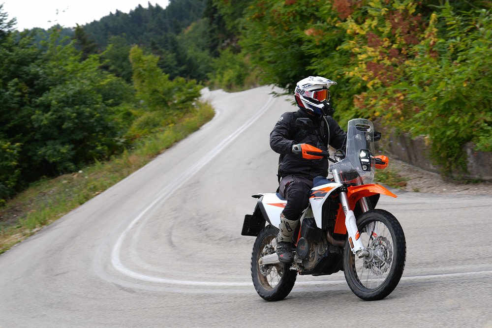 2027 KTM 690 Rally riding through a left-hand turn on a paved road.