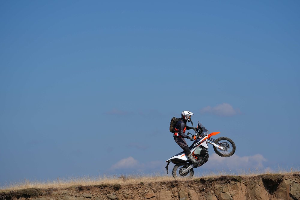 2027 KTM 690 Rally wheelying across a hilltop.