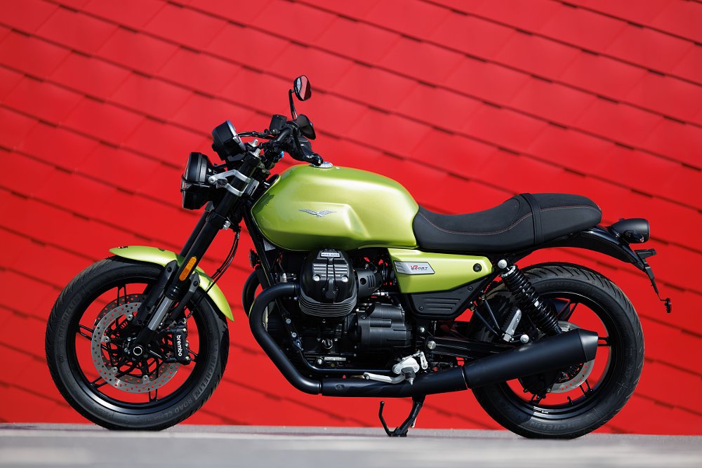 A green Moto Guzzi V7 in front of the red door at the entrance to the factory