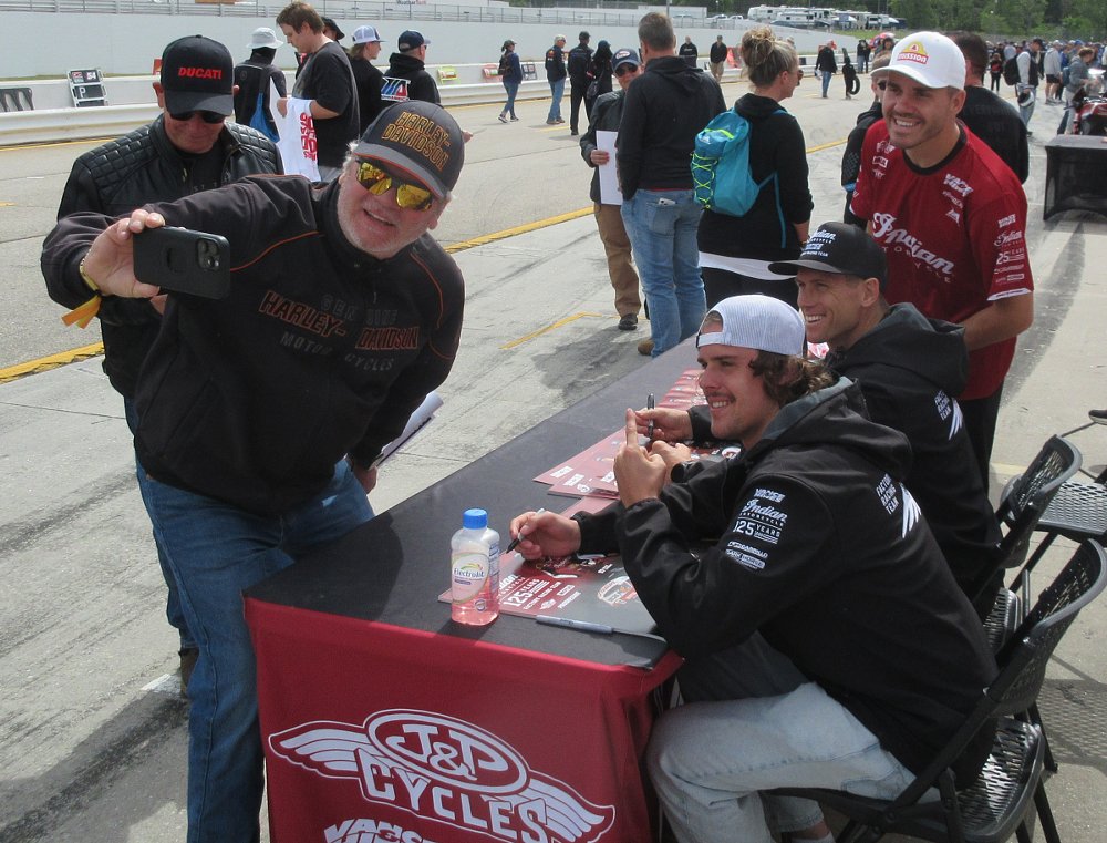a fan wearing a Harley-Davidson hat and sweatshirt taking a selfie with the three Indian Factory Team racers