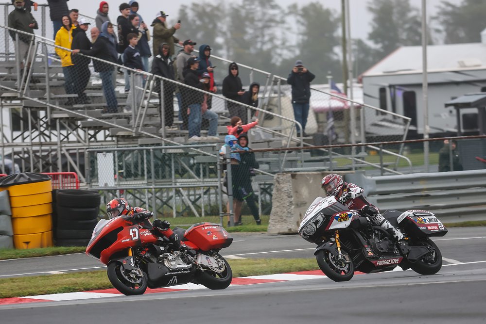 orange Harley-Davidson ahead of a black and white Indian racing in front of fans in rain gear