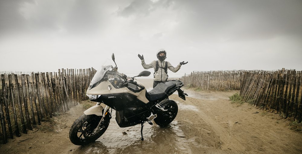 Verstaen beside his motorcycle under gray clouds on wet sand by the shore