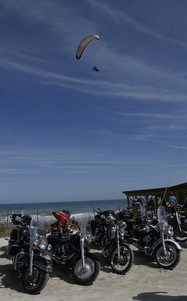 paragliding over the ocean, motorcycles parked at the beach