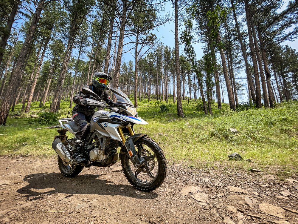 A female rider on the BMW G 310 GS rides on a dirt road in the forest, fish lens camera perspective.