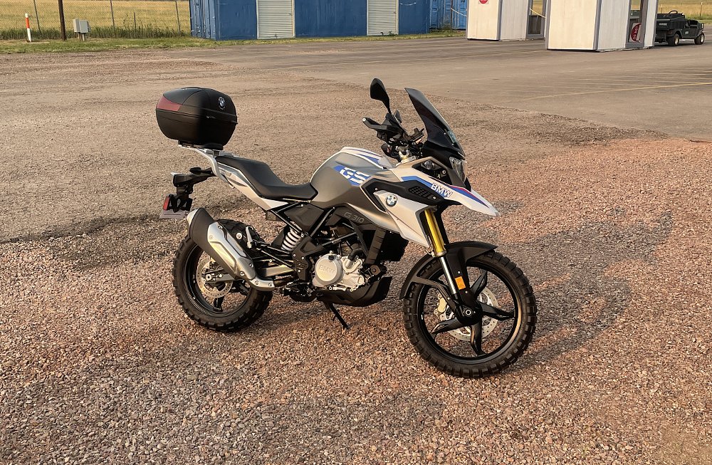 The BMW G 310 GS sits in a gravel driveway with morning light shinning on it.