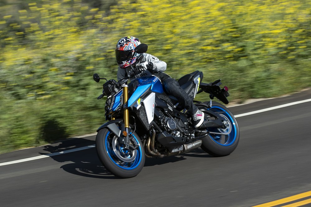 A speed shot of the GSX-S1000 riding through a road surrounded by yellow flowers
