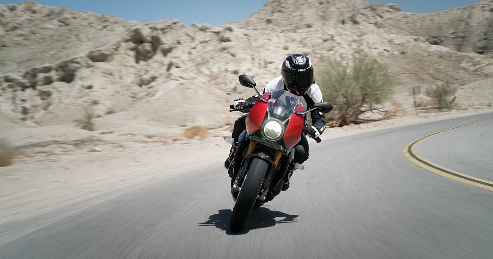 A female rider rides in a desert canyon road on board the Speed Triple 1200 RR