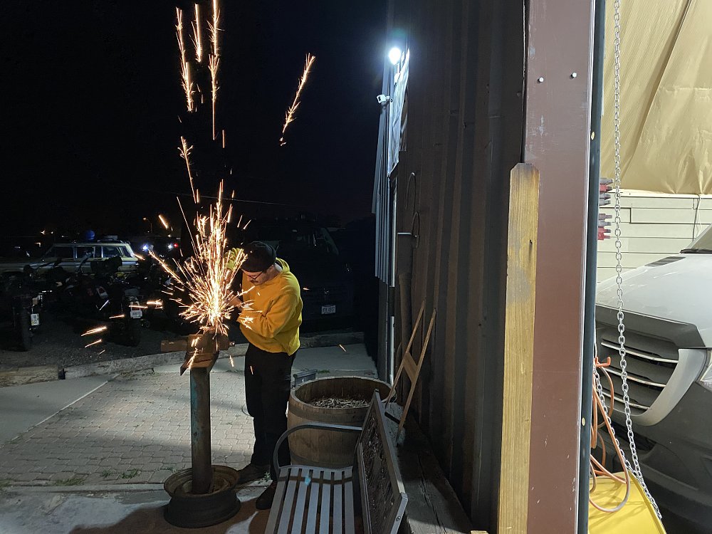 a grinder throws sparks in the dark as a rider makes a repair in camp