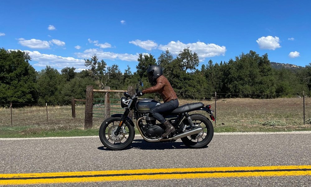 A female rider in profile view as she rides down the road with a big blue sky and green forest in the background