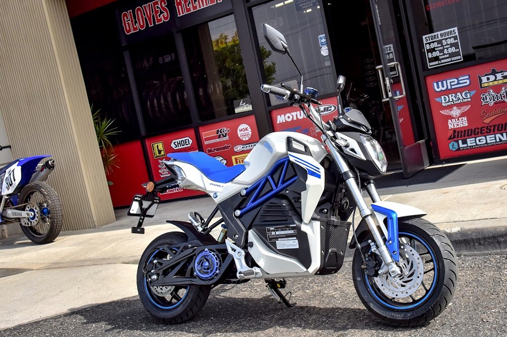 A side view of the CSC City slicker in white and blue that is a mini sized e-motorcycle