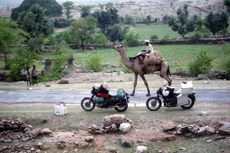 man riding a camel past two parked motorcycles