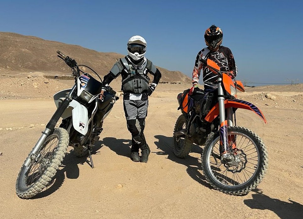 Riders geared up beside dirt bikes, ready to go
