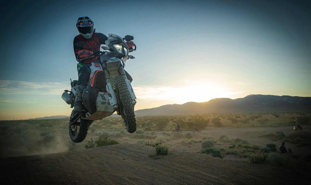 2021 KTM 890 Adventure R Rally jumping over a tabletop on a motocross track with the sun setting in the background.