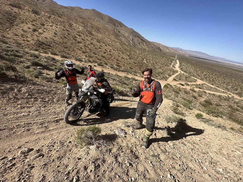 Spurgeon Dunbar standing on a hillside, helping a motorcycle up a steep, sandy hill.