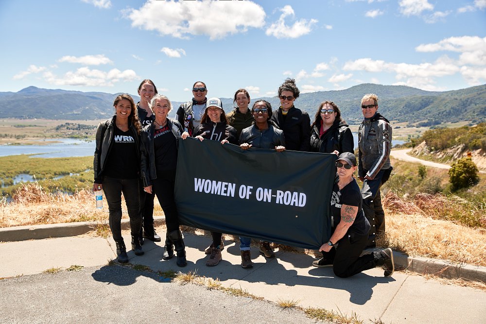 a group of female riders pose at a lakeside overlook with a can-am women riders banner